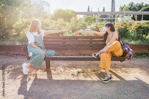 Two friends wearing protective masks sitting on bench during Corona crisis and keeping distance photo