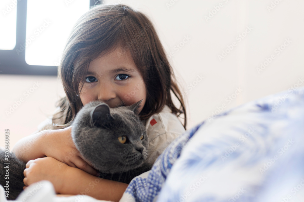 Portrait of little girl cuddling grey cat on bed Portrait of little girl cuddling grey cat on bed