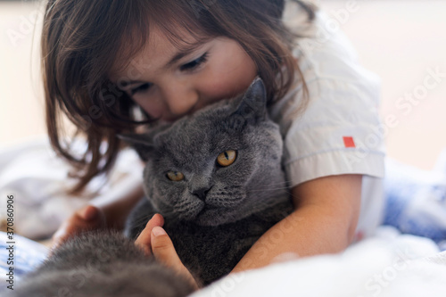 Little girl cuddling grey cat on bed