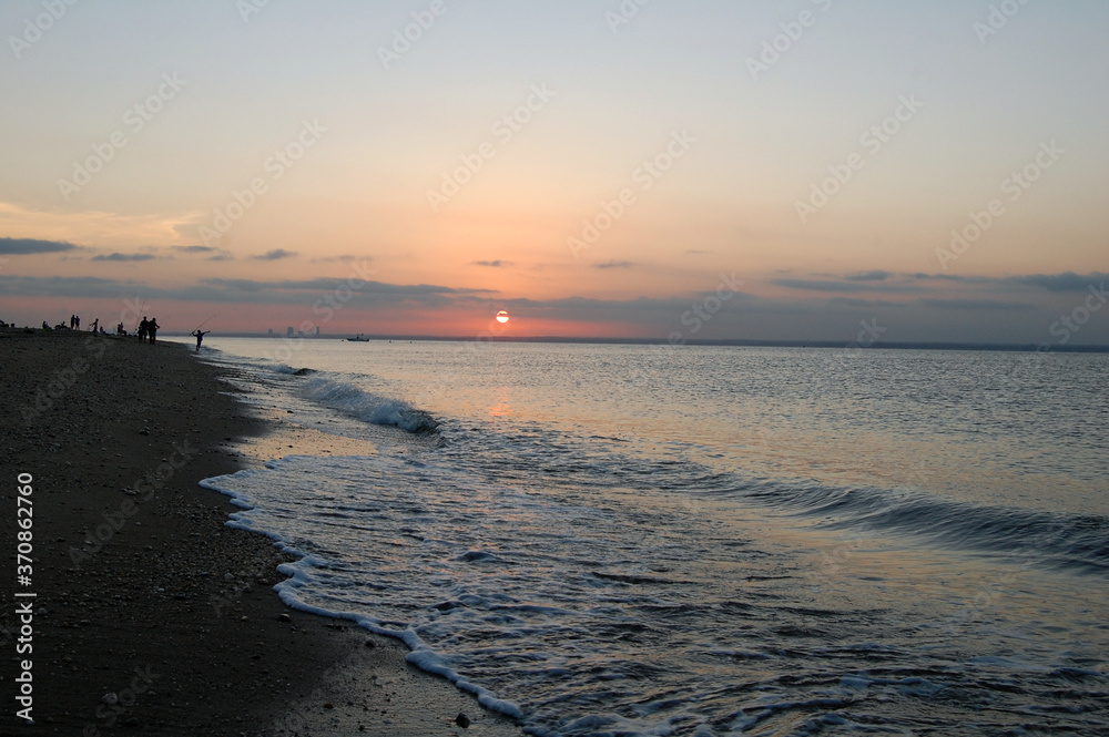 Silhouette of people fishing during the sunset while waves crash on beautiful shoreline