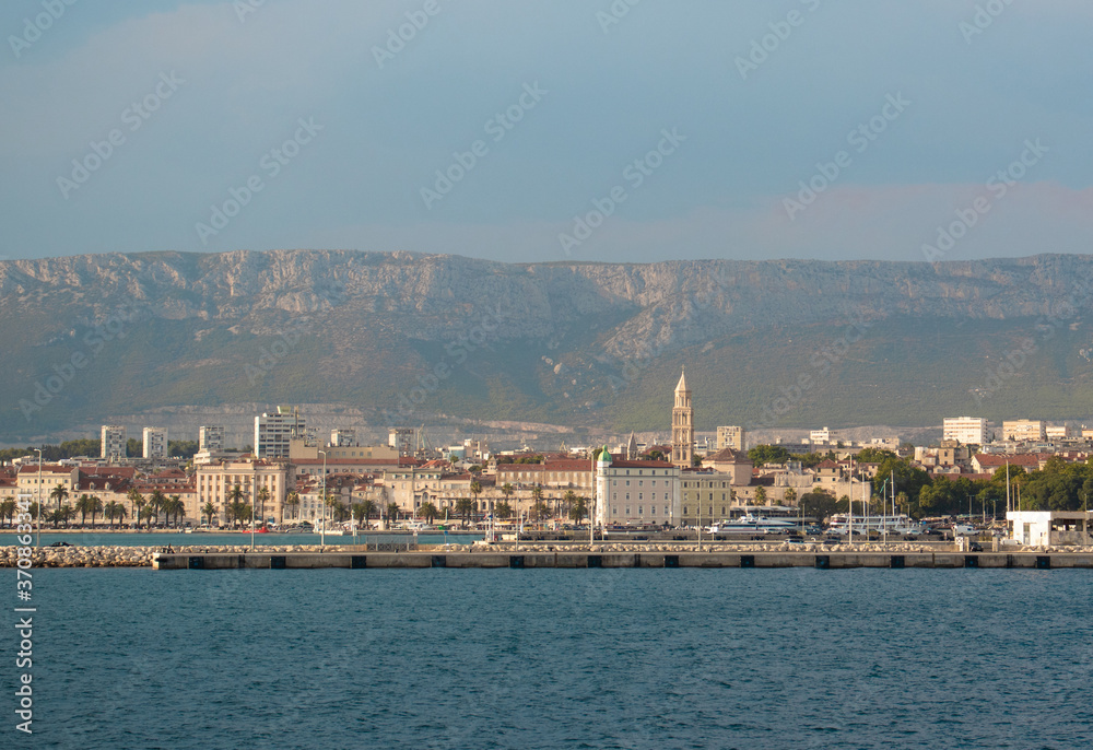 View of Split, Croatia town from a car ferry approaching for very far. Church belltower seen rising above the old buildings, mountains and sky in the distance