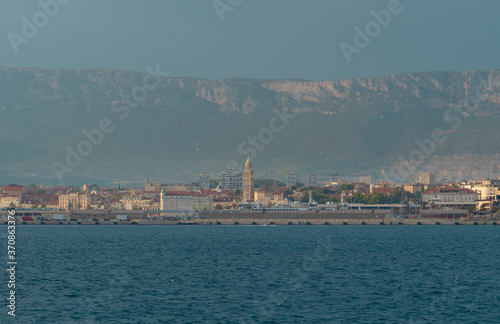 View of Split, Croatia town from a car ferry approaching for very far. Church belltower seen rising above the old buildings, mountains and sky in the distance