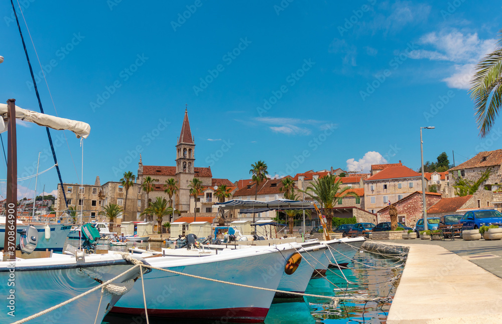 Beautiful panoramic picturesque view of a small town of Milna on the island of Brac. Old boats docked in the crystal clear sea, warm summer day. Old church belltower rising above the buildings
