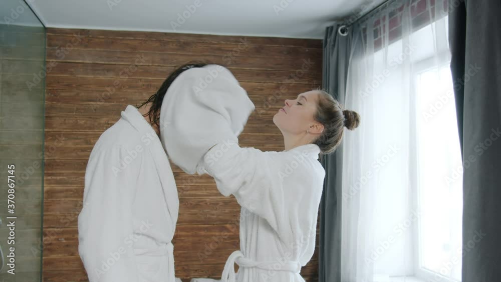 Young woman in bathrobe is drying man's wet hair with towel then kissing in hotel room, newly married couple is enjoying time together. Youth and lifestyle concept.
