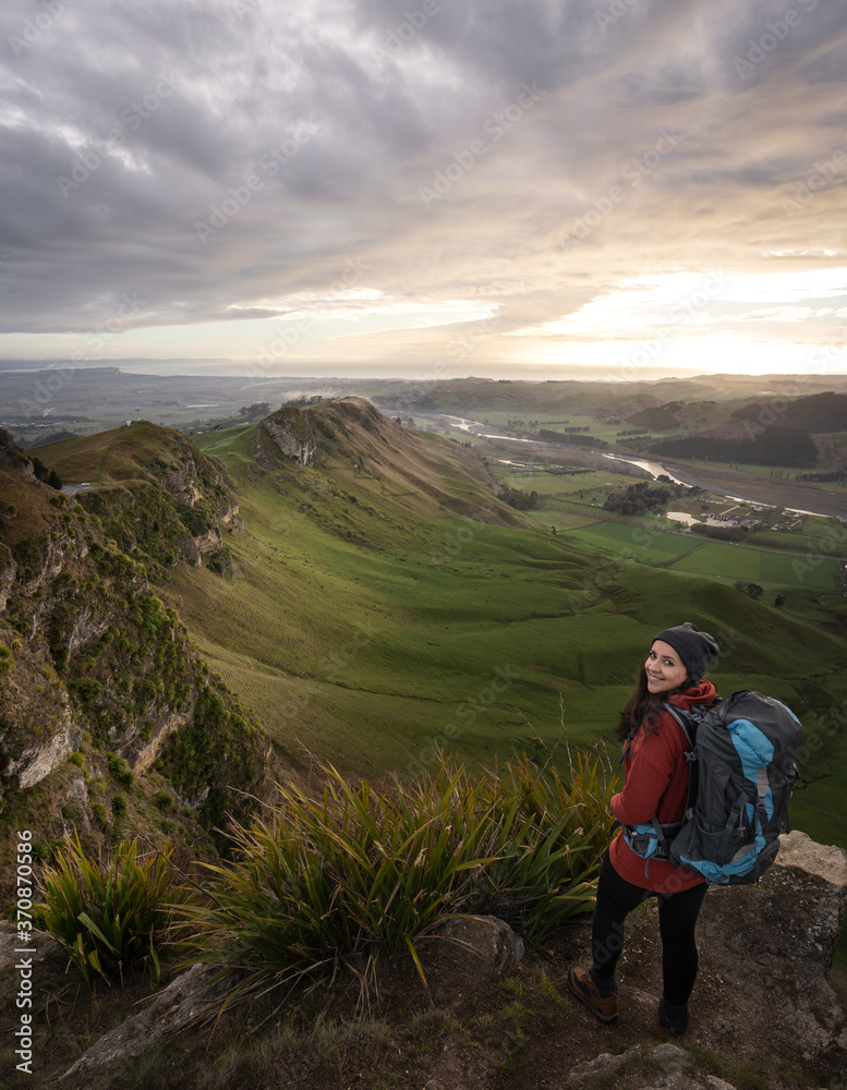 Fototapeta premium Young woman with backpack posing at the top of a mountain. Vertical photography