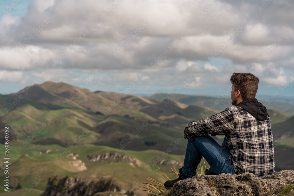 Young man sitting at the top of the mountain and looking at the horizon
