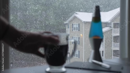 hand picks up glass coffee mug snowing outside apartment building woodstock georgia slow motion photo