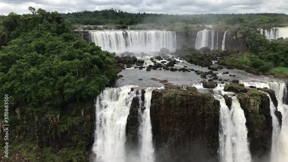 Sensational panoramic scenic landscape view above Iguazu waterfalls cascading down rocky mountains on cloudy day, handheld pan left Sensational panoramic scenic landscape view above Iguazu waterfalls cascading down rocky mountains on cloudy day, handheld pan left