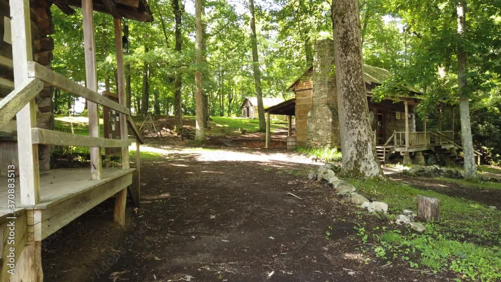 Old historic log cabin village in forest with green trees and dirt pathway on sunny day, Boone, North Carolina, America, handheld pan up Old historic log cabin village in forest with green trees and dirt pathway on sunny day, Boone, North Carolina, America, handheld pan up