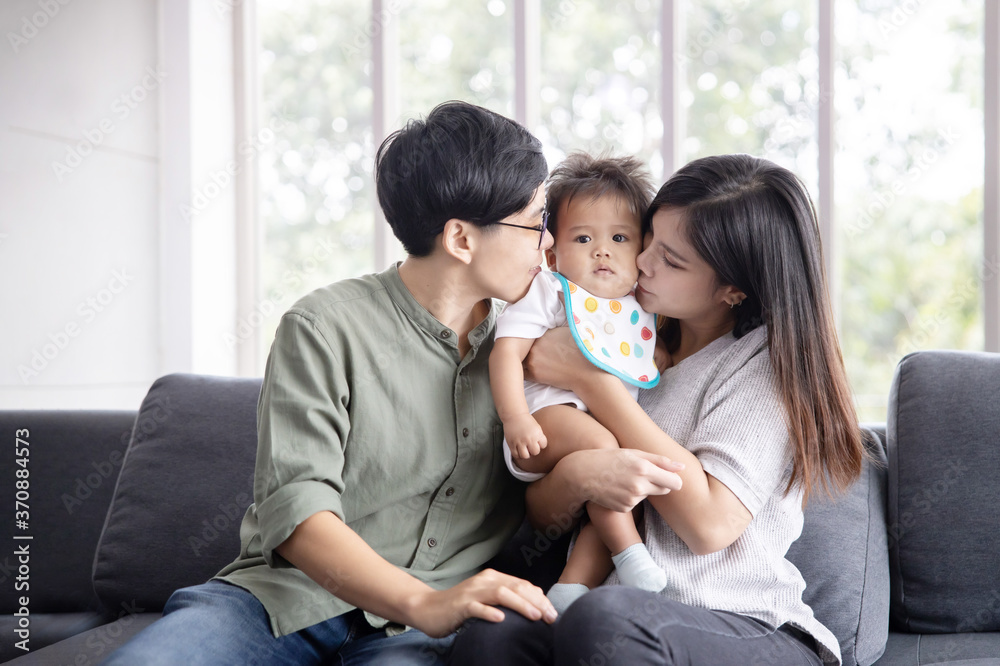 Asian lesbian couple kissing their adopted baby on both cheecks