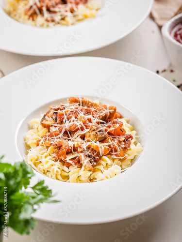 Close-up Fusilli with mushrooms in tomato sauce in a white plate. Classic Mediterranean recipes. Traditional Italian pasta. Tomato sauce, mushrooms, spices and Parmesan cheese. Vertical shot
