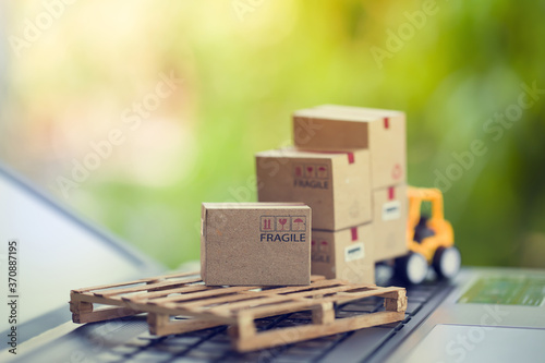 Logistic and cargo freight concept: Fork-lift a truck moves a paper box on notebook keyboard in the natural green background. depicts  International freight or shipping service for online shopping.