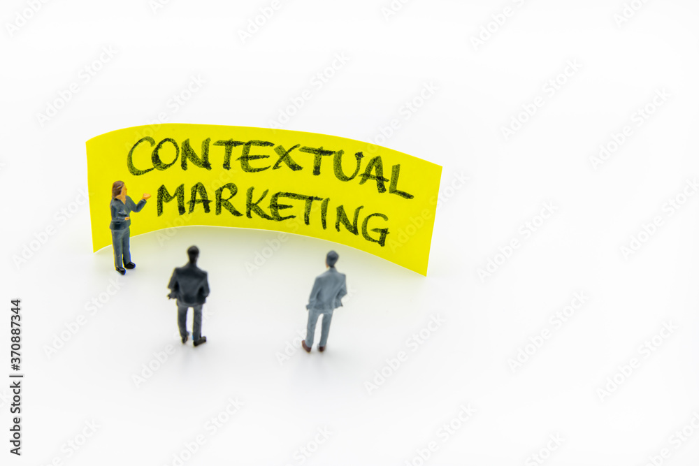Presentation meeting with miniature figurines posed as business people standing in front of post-it note with Contextual Marketing handwritten message in background, copy space on the right Presentation meeting with miniature figurines posed as business people standing in front of post-it note with Contextual Marketing handwritten message in background, copy space on the right