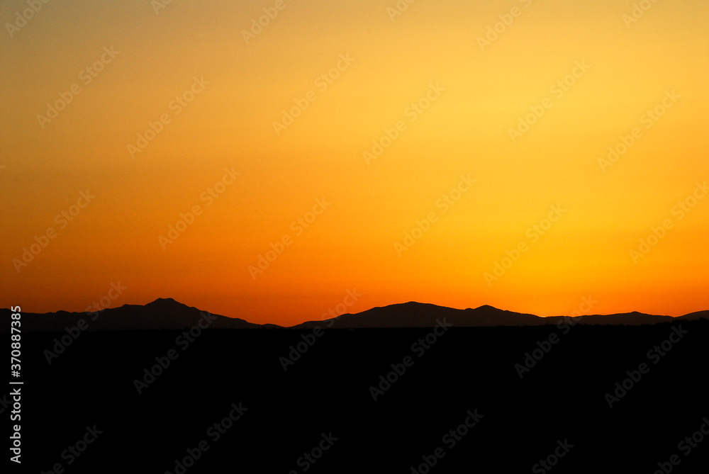 Orange sunset with panoramic view of mountains silhouette against orange sky