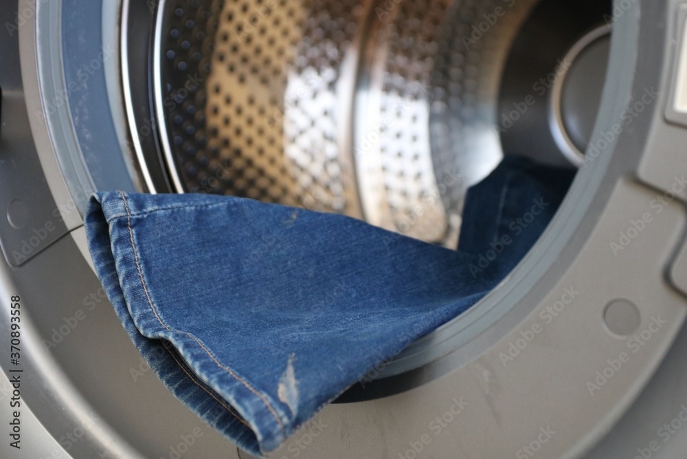 Open door in washing machine with dirty jeans inside close up Open door in washing machine with dirty jeans inside close up