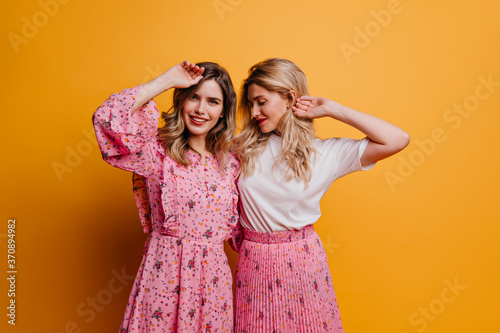Glamorous woman in cute pink dress spending leisure time with sister. Indoor photo of amazing female models expressing positive emotions.