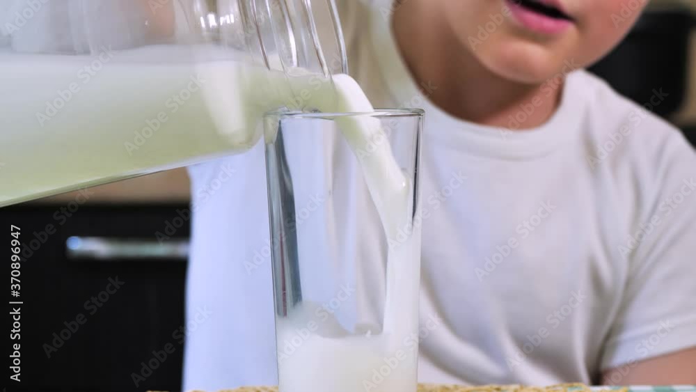 Boy pours milk in a transparent glass from jug Boy pours milk in a transparent glass from jug