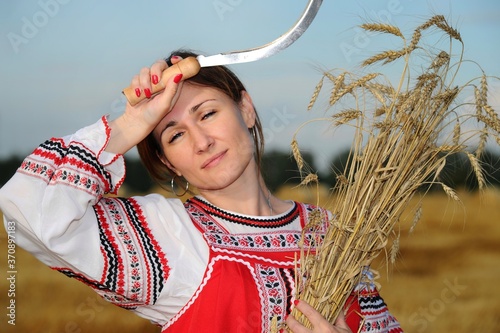 Peasant girl in national costume from a white shirt and a red sundress on the field during the harvest
