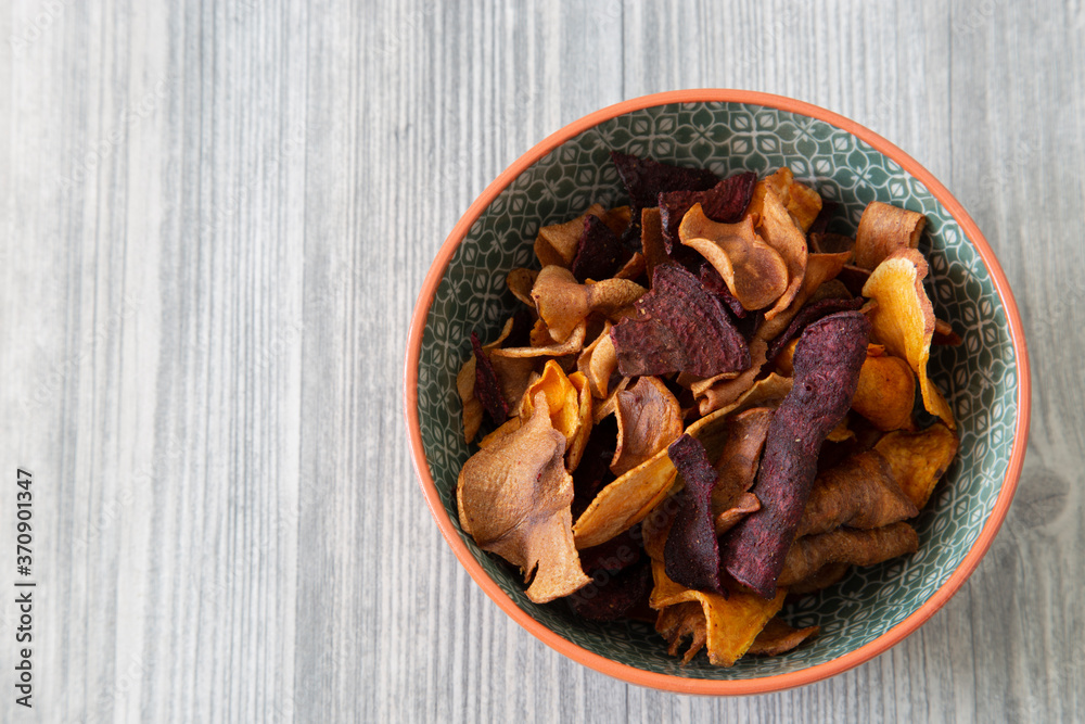 Sweet potato, beetroot and parsnip crisps chips in a patterned bowl. Grey wood background Sweet potato, beetroot and parsnip crisps chips in a patterned bowl. Grey wood background