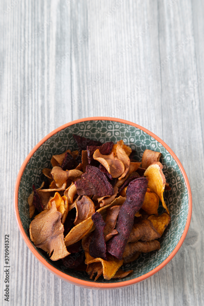 Sweet potato, beetroot and parsnip crisps chips in a patterned bowl. Grey wood background Sweet potato, beetroot and parsnip crisps chips in a patterned bowl. Grey wood background