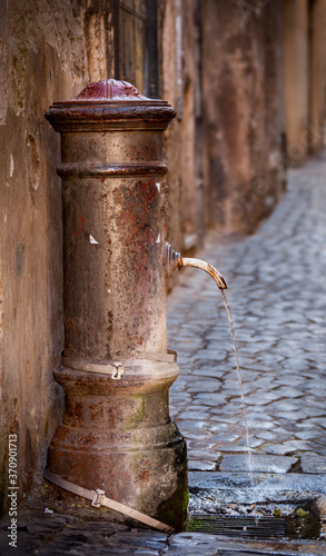 A vintage drinking fountain water spout provides continuous fresh water for thirsty travelers in a back alley in Rome, Italy.