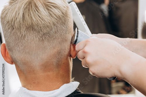 A handsome blond man of European appearance is doing a haircut. Close-up photo. Man at the barber shop