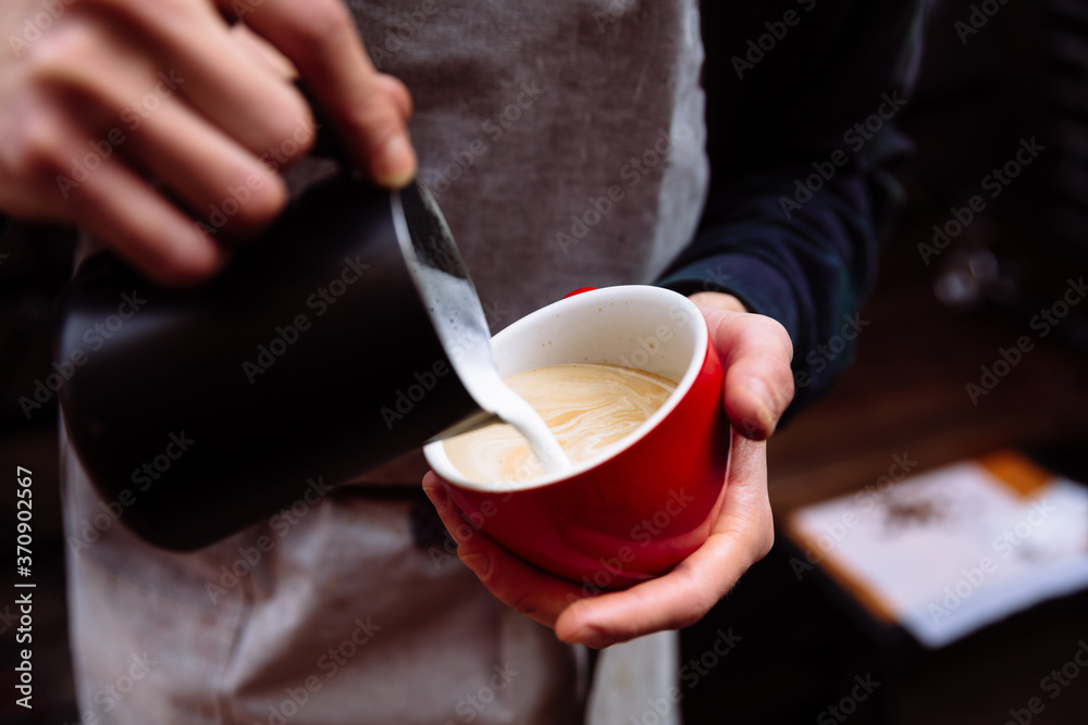 Barista pours fresh milk into a cup of coffee. Flower Latte art.