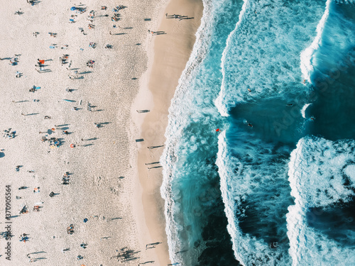 Aerial view of the sea in Australia. Summer seascape with people sunbathing on the beach, under umbrellas, beautiful waves, rocks and sand, turquoise water. Top view from drone
