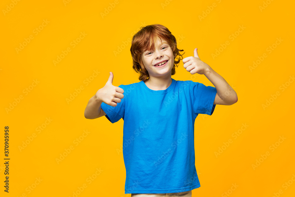 boy red hair blue t-shirt yellow isolated background freckles and a happy look from the thumb boy red hair blue t-shirt yellow isolated background freckles and a happy look from the thumb