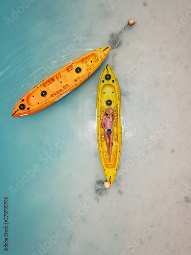 Two kayaks with a woman sunbathing in a swimsuit and a hat, perfect body under the palm trees on the blue ocean water close to the white sand beach