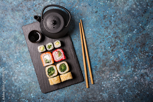 Set of sushi rolls served on a black slate board with chopsticks and asian teapot