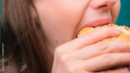 Close up of a female biting a burger on a green screen. The concept of unhealthy nutrition and diet.