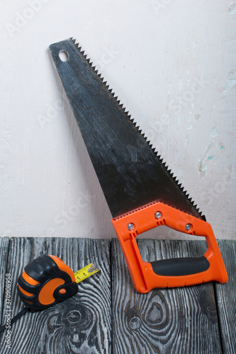 A hacksaw and measuring tape lie on painted pine boards.