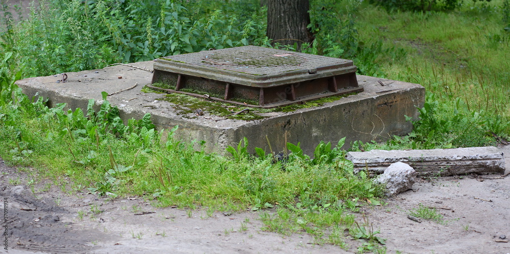An old concrete manhole with a metal cover in the green grass An old concrete manhole with a metal cover in the green grass