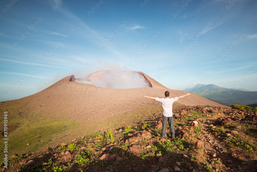 Tourist enjoying freedom facing active volcano Telica with the first light of dawn and sulfuric smoke rising from the volcanic cone