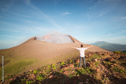 Obraz na płótnie Tourist enjoying freedom facing active volcano Telica with the first light of dawn and sulfuric smoke rising from the volcanic cone w salonie