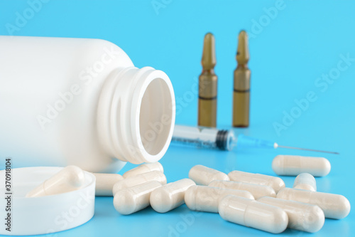 Pills, capsules, syringe, White medical containers, ampoules on blue background. Medical vial for injection with a syringe. Medical background photo