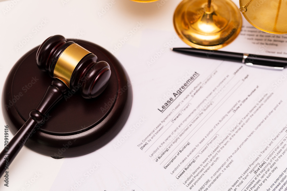 Concept of lease law or tenancy law: the cover of lease agreement was is placed near the blurred wooden gavel and law scales.