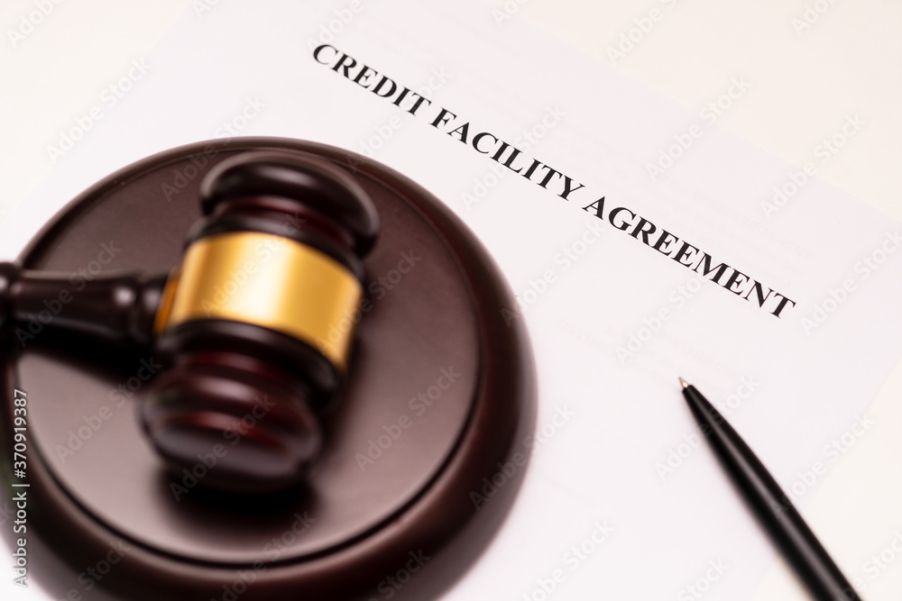 Concept of banking, finance and commercial laws: the cover of credit facility agreement is placed near the wooden gavel and pen. The company name is a supposed name