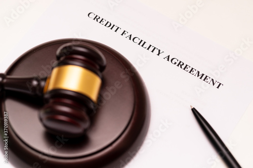 Concept of banking, finance and commercial laws: the cover of credit facility agreement is placed near the wooden gavel and pen. The company name is a supposed name