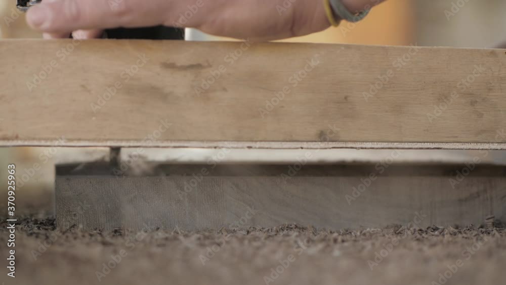 Close-up. A Joinery cuts an old walnut wood plank with an electric hand-held fraser Close-up. A Joinery cuts an old walnut wood plank with an electric hand-held fraser
