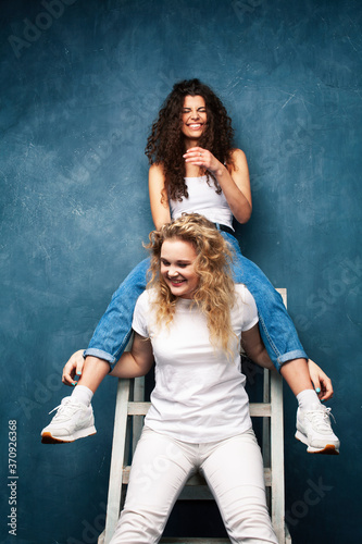 young pretty teenage girls friends with blond and brunette curly hair posing cheerful on blue background, lifestyle people concept