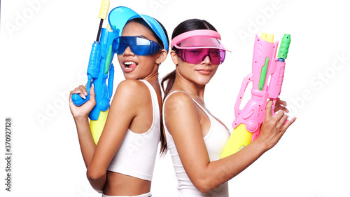 Portrait of two beautiful Asian women in pink and blue sun visor cap and sunglasses posing with water guns over white background