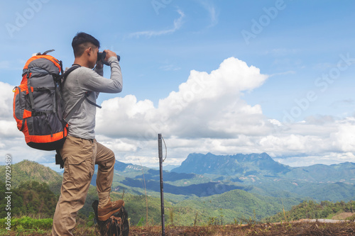 Young man with backpack and holding a binoculars looking on top of mountain