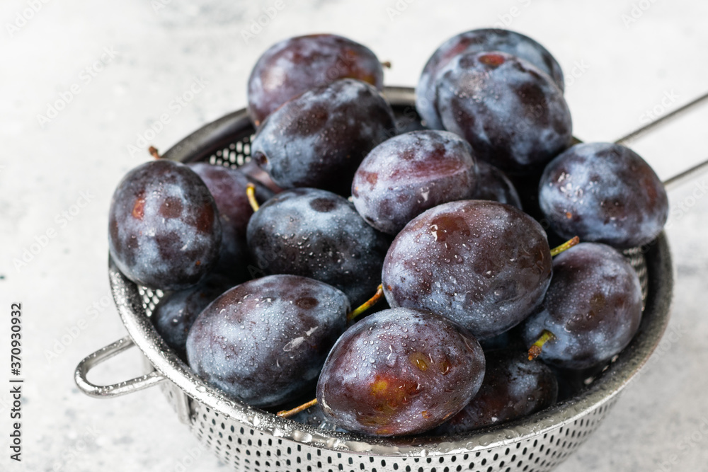 Obraz premium Ripe plum. Lots of plums in a metal bowl on a light background. Blue plums close-up. Healthy fruits