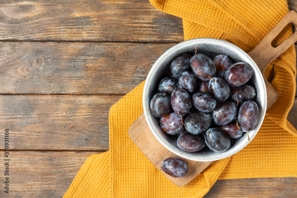 Ripe plum. Lots of plums in a metal bowl on a brown wooden table. Blue plums in a bowl. Top view with a space for text. Healthy fruits Ripe plum. Lots of plums in a metal bowl on a brown wooden table. Blue plums in a bowl. Top view with a space for text. Healthy fruits
