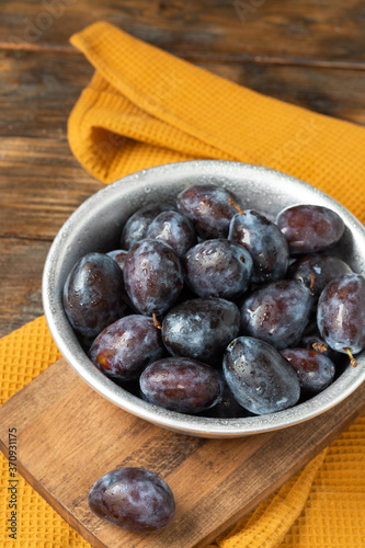 Ripe plum. Lots of plums in a metal bowl on a brown wooden table. Blue plums in a bowl close-up. Healthy fruits