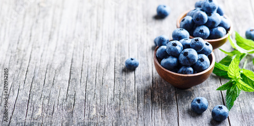 Bowl of fresh blueberries on blue rustic wooden table closeup.