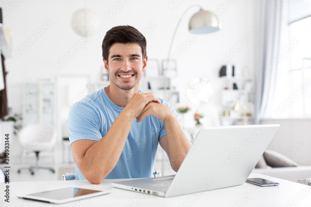 Handsome smiling man with a laptop at office desk.
