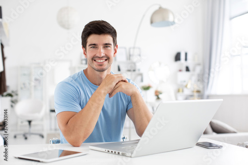 Handsome smiling man with a laptop at office desk. © BestForYou